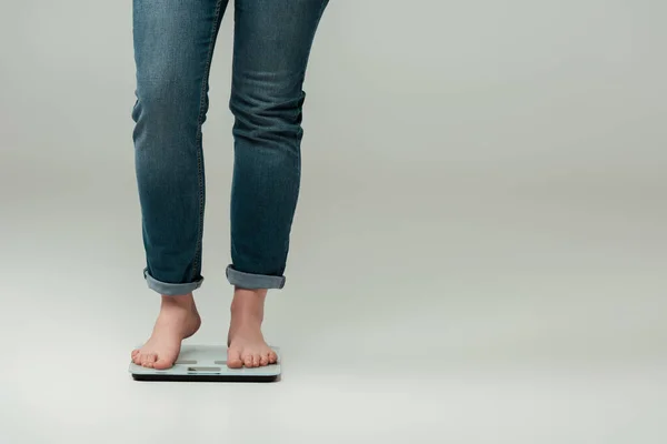Обрезанный вид плюс размер девушка в джинсах стоя на весах на сером — стоковое фото