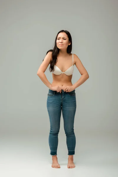 Displeased and overweight asian girl wearing jeans on grey — Stock Photo