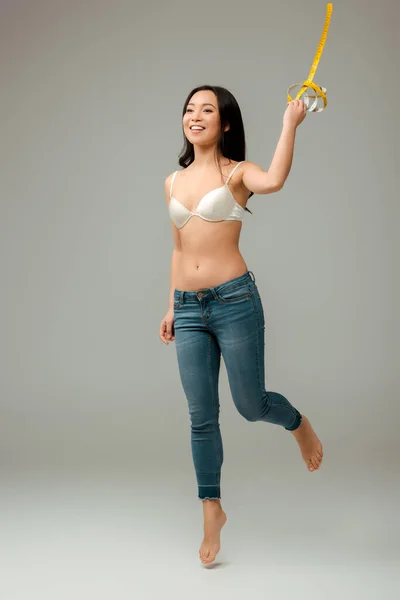 Cheerful and overweight asian girl holding measuring tape and jumping on grey — Stock Photo