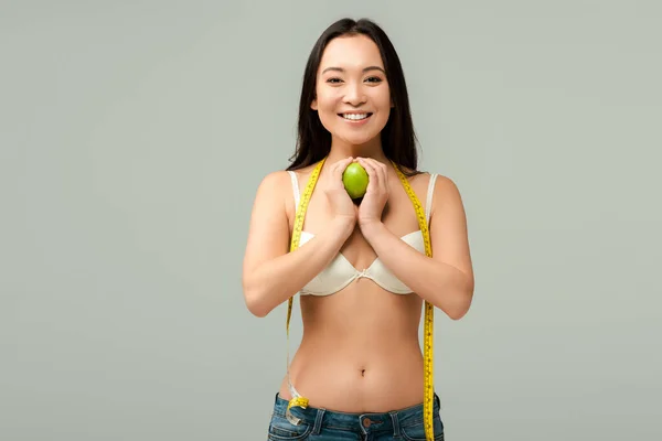 Sonriente y con sobrepeso asiático chica holding manzana aislado en gris - foto de stock