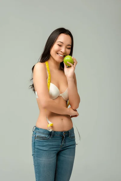 Smiling and overweight asian girl in bra holding apple isolated on grey — Stock Photo