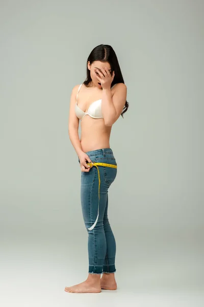 Scioccato e in sovrappeso asiatico ragazza in reggiseno misurazione fianchi e copertura faccia su grigio — Foto stock