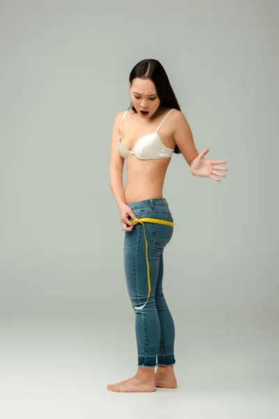 Shocked and overweight asian girl in bra measuring hips on grey — Stock Photo
