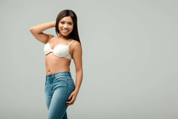Overweight and cheerful african american girl in jeans and bra isolated on grey — Stock Photo