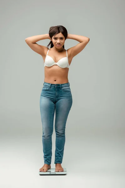 Donna afroamericana sovrappeso in jeans e reggiseno in piedi su squame e capelli toccanti su grigio — Foto stock