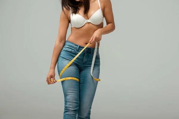 Cropped view of overweight african american girl in jeans and bra measuring thigh isolated on grey — Stock Photo