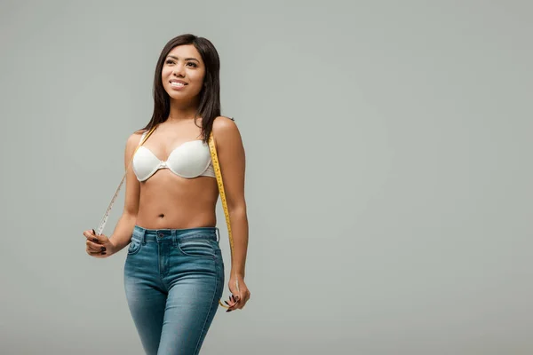 Happy and overweight african american girl in jeans and bra standing with measuring tape isolated on grey — Stock Photo