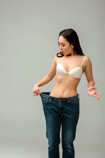 Surpresa asiático mulher no oversized jeans isolado no cinza — Fotografia de Stock