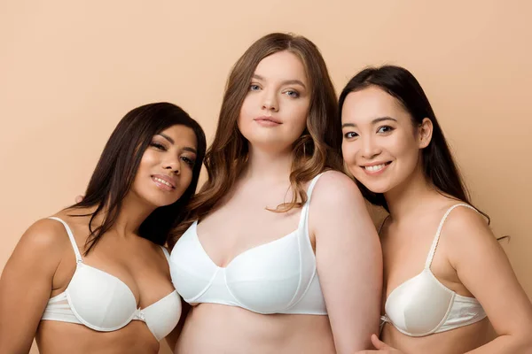 Happy and overweight multicultural women in bras isolated on beige — Stock Photo