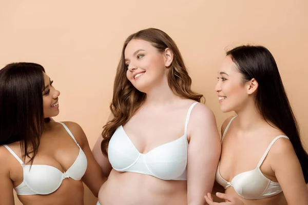 Fröhliche und übergewichtige multikulturelle Frauen in BHs isoliert auf beige — Stockfoto