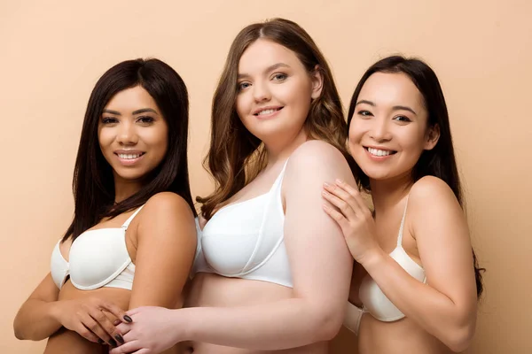 Mujeres multiculturales sonrientes y con sobrepeso en sostenes aislados en beige - foto de stock