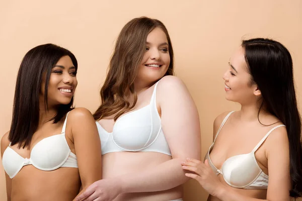 Feliz más tamaño mujeres multiculturales en sujetadores aislados en beige - foto de stock