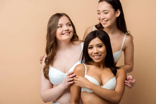Smiling plus size multicultural women in bras isolated on beige — Stock Photo