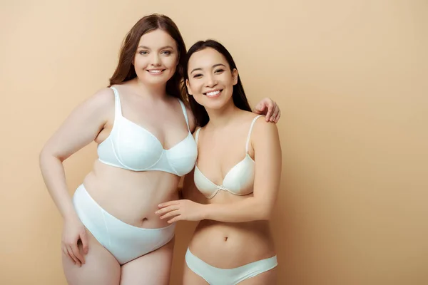 Plus size woman smiling with asian girl in underwear isolated on beige, body positive concept — Stock Photo