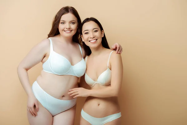 Más tamaño mujer sonriendo con asiático chica en ropa interior aislado en beige, cuerpo positivo concepto - foto de stock