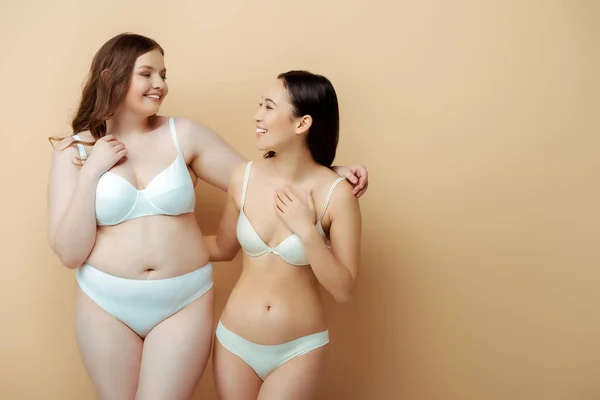 Happy plus size woman standing with asian girl in underwear isolated on beige, body positive concept — Stock Photo