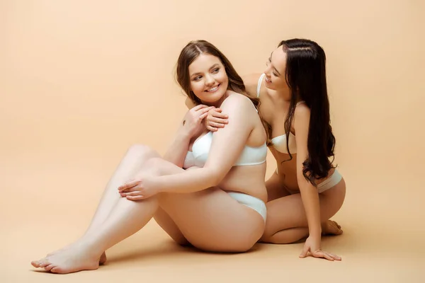 Asiatico ragazza abbracciare felice in sovrappeso donna in biancheria intima mentre seduta su beige corpo positivo concetto — Foto stock