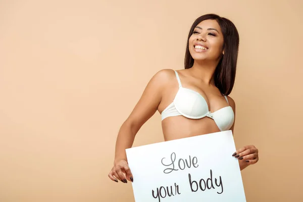 Feliz afro-americana segurando cartaz com amor seu corpo lettering isolado no bege — Fotografia de Stock