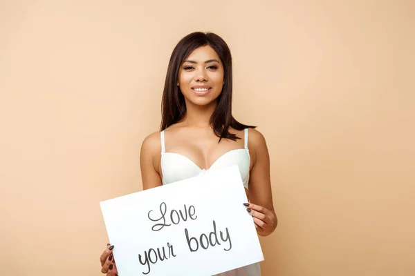 Весела афроамериканська дівчина тримає плакат з любов'ю до вашого тіла, що розкладається ізольовано на бежевому — стокове фото