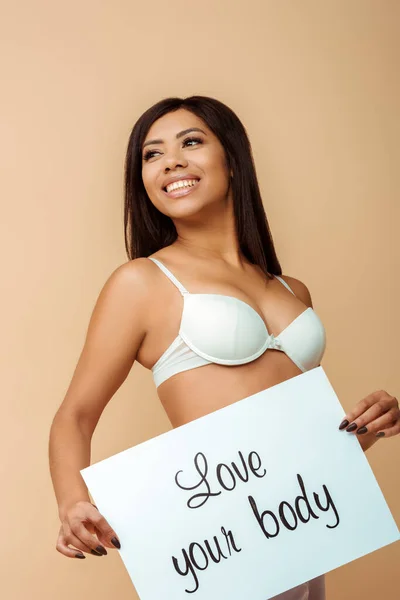 Glücklich afrikanisch-amerikanische Mädchen hält Plakat mit Liebe Ihren Körper Schriftzug isoliert auf beige — Stockfoto