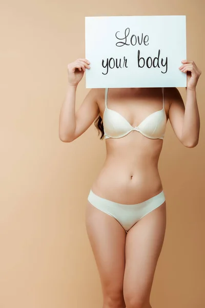 Young woman covering face while holding placard with love your body lettering isolated on beige — Stock Photo