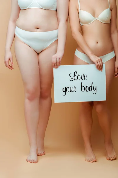 Vista recortada de las mujeres con pancarta con amor su cuerpo letras sobre fondo beige - foto de stock