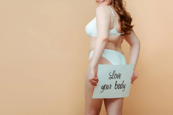 Cropped view of plus size woman presenting placard with love your body inscription isolated on beige — Stock Photo