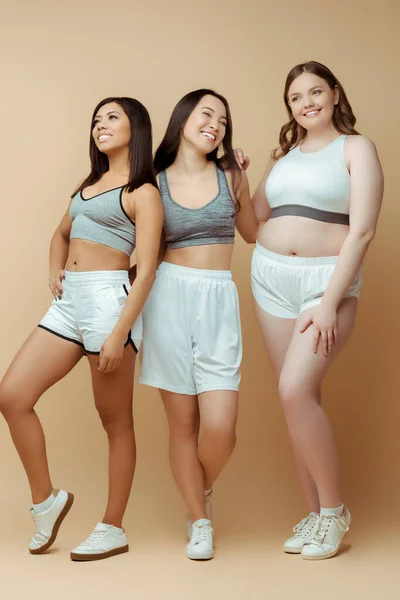 Deportivas multiétnicas en ropa deportiva sonriendo sobre fondo beige - foto de stock