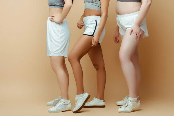 Cropped view of multicultural sportswomen in shorts on beige — Stock Photo