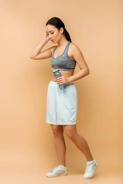 Asian sportswoman holding sports bottle on beige background — Stock Photo