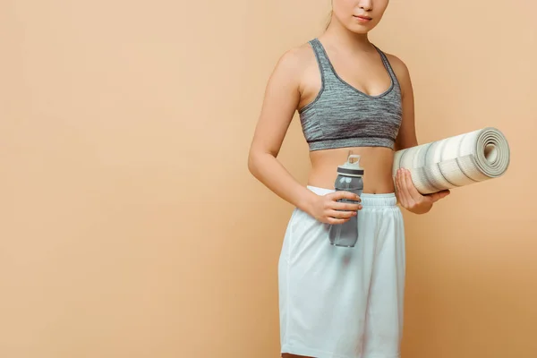 Vista recortada de la deportista con tapete de fitness y botella deportiva en beige - foto de stock