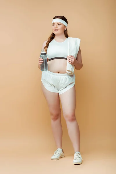 Plus-Size-Sportlerin mit Handtuch und Sportflasche schaut beige weg — Stockfoto