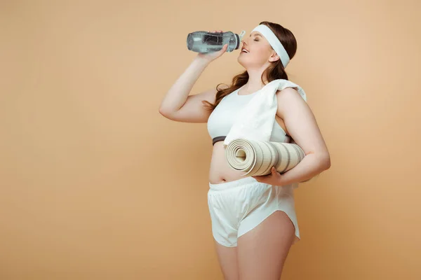 Плюс размер: женщина с фитнес-ковриком, питьевая вода бежевого цвета — стоковое фото