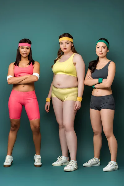 Multiethnic sportswomen with crossed arms looking at camera on green — Stock Photo