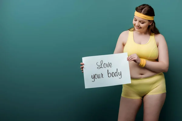 Plus-Size-Sportlerin lächelt und betrachtet Plakat mit Liebe zum Körper Schriftzug auf Grün — Stockfoto