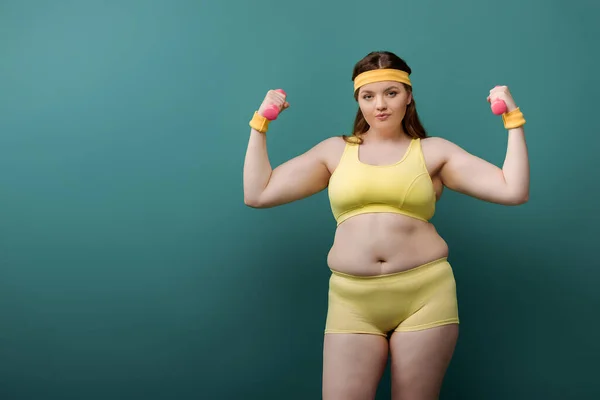 Plus size sportswoman olhando para a câmera com halteres no fundo verde — Fotografia de Stock