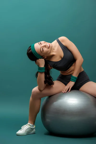 Attraktive asiatische Sportlerin lächelt und schaut auf Fitnessball auf Grün — Stockfoto