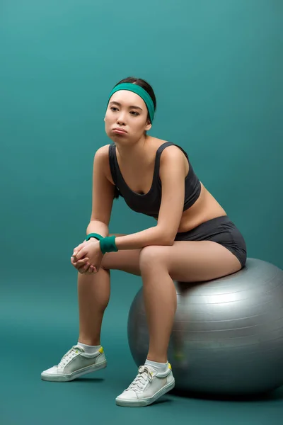 Уставшая азиатская спортсменка сидит на фитнес-мяче на зеленом фоне — стоковое фото