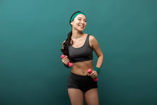 Щаслива азіатська спортсменка з гантелями посміхається ізольовано на зеленому — стокове фото