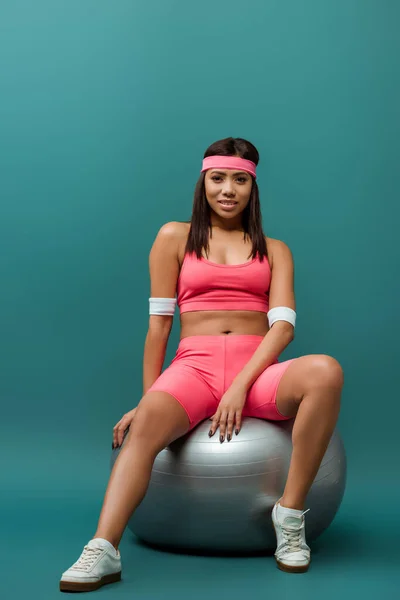 Afroamericana deportista en ropa deportiva rosa sonriendo y mirando a la cámara sobre fondo verde - foto de stock