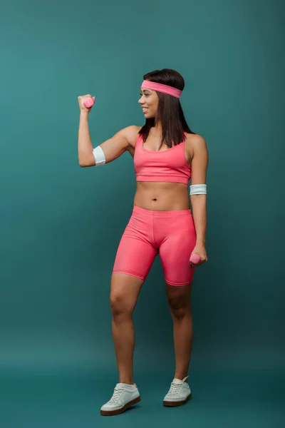 African american sportswoman smiling and looking at dumbbell on green background — Stock Photo