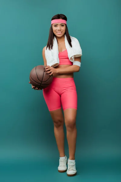 Африканская американская спортсменка улыбается и смотрит в камеру с полотенцем и мячом на зеленом — стоковое фото