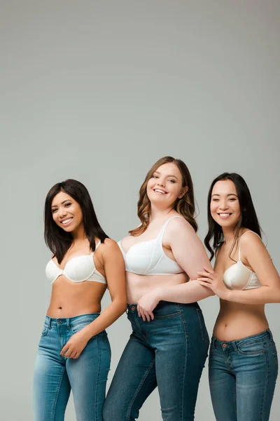 Multicultural women smiling and looking at camera isolated on grey — Stock Photo