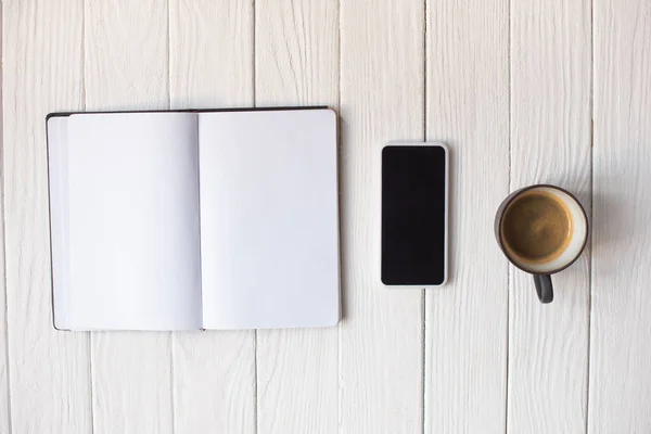 Top view of cup of coffee, smartphone and notebook on wooden background — Stock Photo