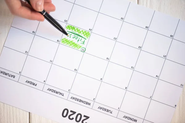 Ausgeschnittene Ansicht einer Frau, die mit Stift auf Fitness-Schriftzug im To-Do-Kalender mit der Aufschrift 2020 auf Holzgrund zeigt — Stockfoto