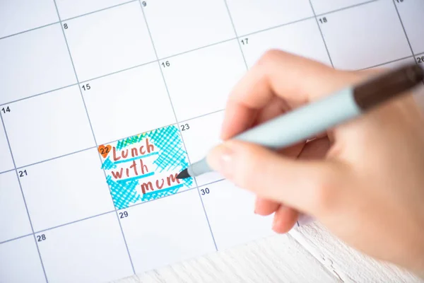 Vista ritagliata della donna che punta con pennarello a pranzo con scritta mamma nel calendario da fare su sfondo di legno — Foto stock