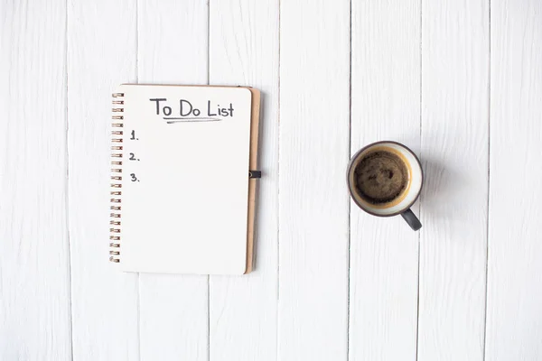 Vista superior do notebook com para fazer lista de letras e xícara de café em fundo de madeira — Fotografia de Stock