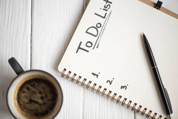 Vista superior del cuaderno con letras de lista de tareas y pluma con taza de café sobre fondo de madera - foto de stock