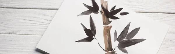 Top view of paper with Japanese painting with bamboo and leaves on wooden background, panoramic shot — Stock Photo