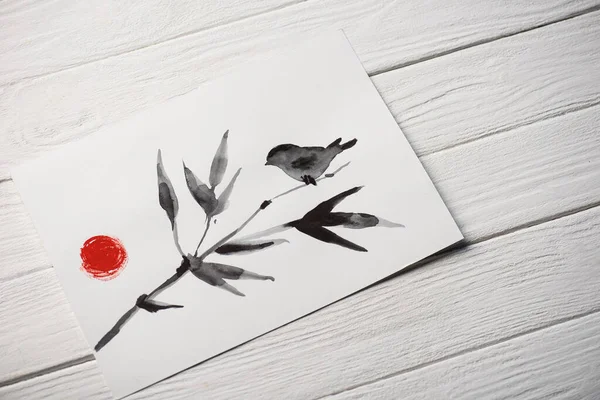 Vista de alto ángulo de papel con pintura japonesa con pájaro en rama y sol sobre fondo de madera - foto de stock
